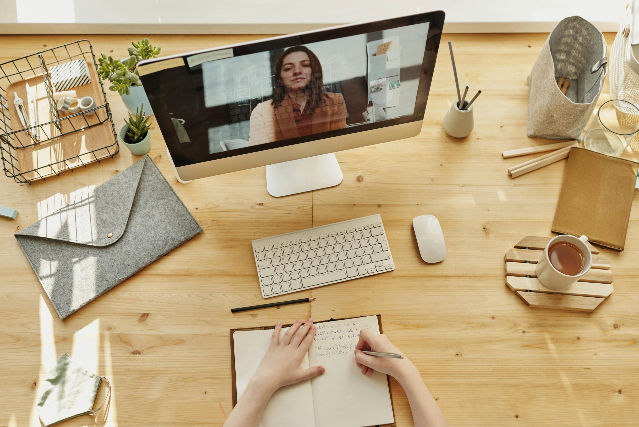 Home Person taking notes during a video call at a neatly organized home desk, showing remote work lifestyle.