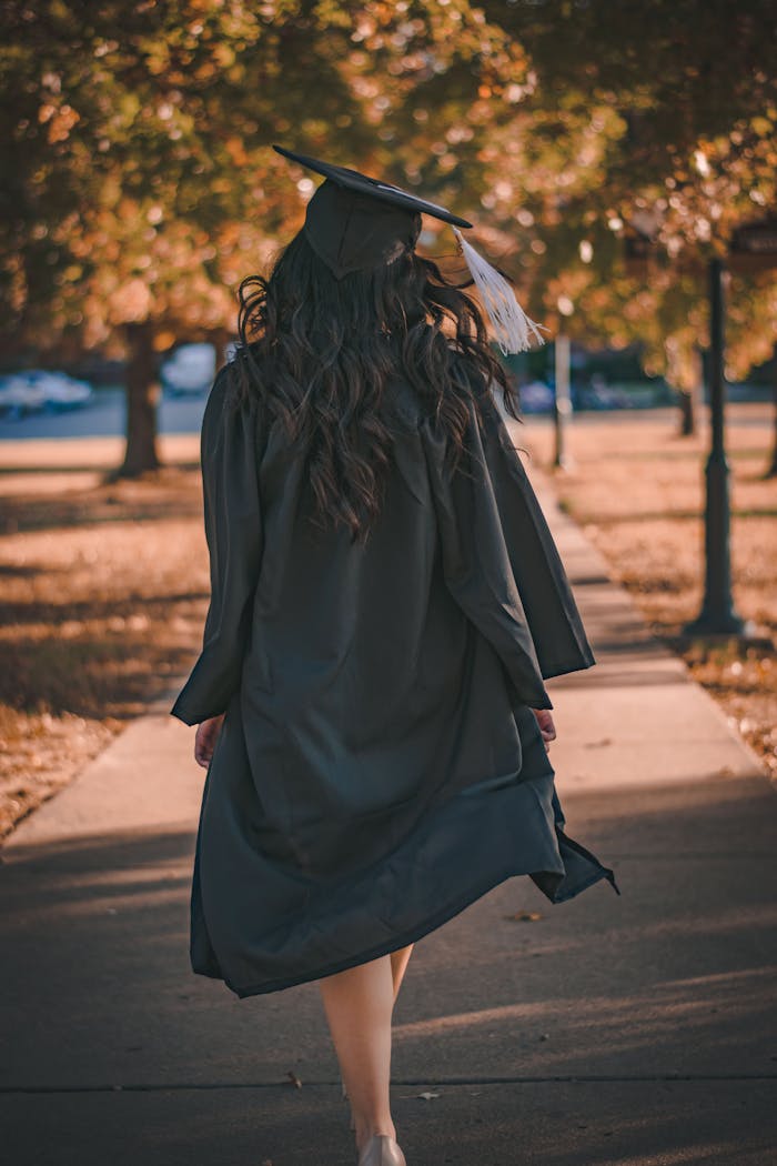 services-04 Back view of a graduate walking in an autumn park in academic dress.